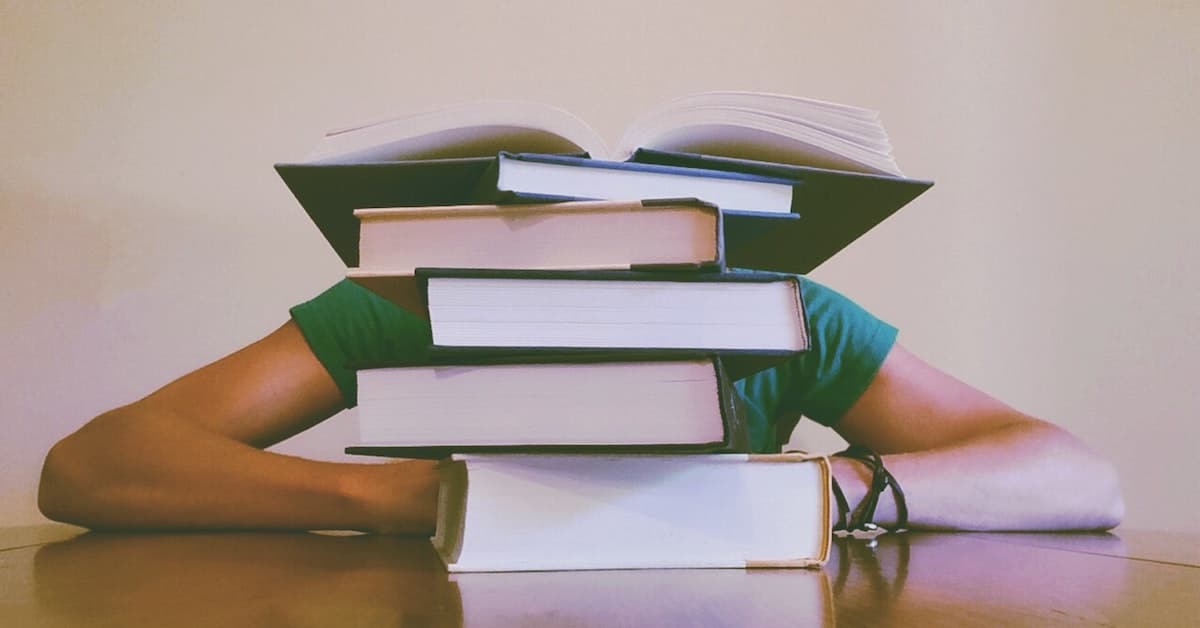 person behind stack of books studying coursework to become a property manager