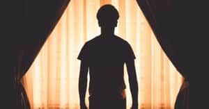 silhouette of male holdover tenant in front of blinds and curtains